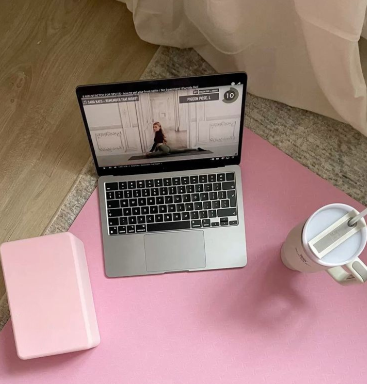 Laptop on a pink surface with a notebook and a cup nearby.